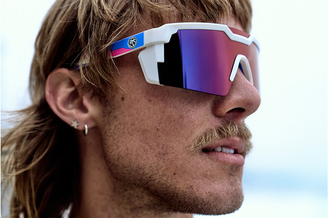 Surfer wearing the Heat Wave Visual Future Tech Sunglasses with gloss white frame, wild print arms and atmosphere lens.