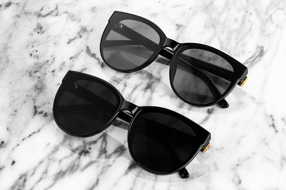 Lying on a table are the Carat Ultra Black Sunglasses in comparison to the Carat Black Sunglasses.