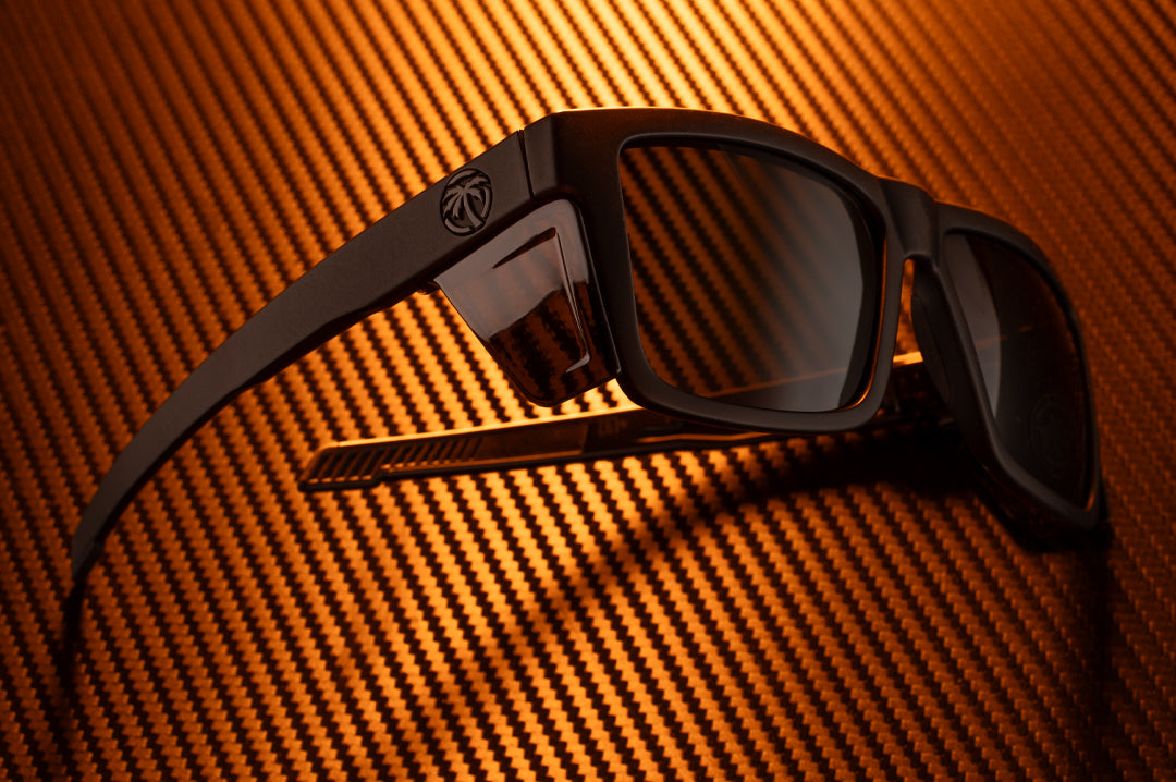 Laying on a table is the Heat Wave Visual Performance Vise Sunglasses with black frame and ultra black lenses.