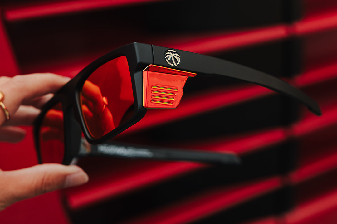 Hand holding up the Heat Wave Visual Performance Rayth Sunglasses with Firestorm red lenses.